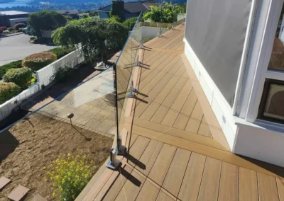 Luxury composite decking with a diagonal board pattern and frameless glass railing overlooking a territorial view.