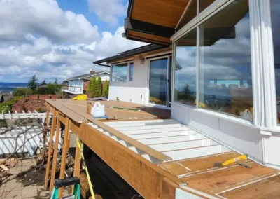 A luxury home deck under construction featuring composite board installation, structural framing, and a vaulted wood soffit.