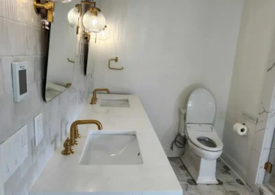 Modern white oak double vanity with quartz countertops and brushed gold widespread faucets.