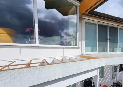 White-painted deck beams and joists during the structural framing phase of an exterior remodel.