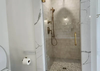 Walk-in shower interior with gold rain shower head and textured Zellige wall tiles.