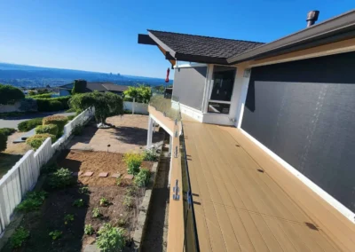 Elevated view of a long composite deck featuring glass railings and deployed retractable solar shades.