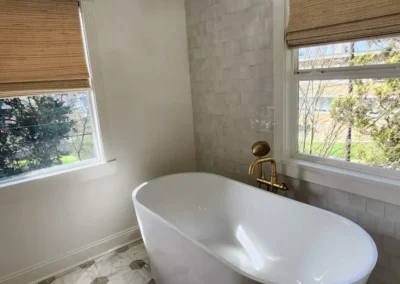 A freestanding tub centered between two windows with woven shades in a luxury bathroom.