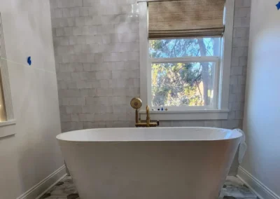 A white freestanding soaking tub positioned under a crystal branch chandelier in a luxury Seattle bathroom.