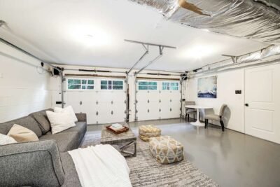 home ADU garage transformation A cozy basement lounge area from an ADU conversion project with a sectional sofa, ottomans, and a table, featuring ductwork and ample lighting.