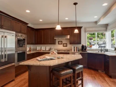 Mercer-Island-Estate-Kitchen-reonovation Open-concept kitchen featuring dark wood cabinetry, a stone-top island with seating, and a large window overlooking a terraced garden.