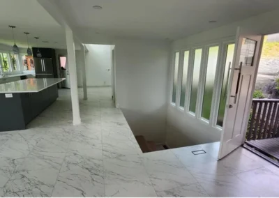 Home entryway with marble-veined tile flooring, staircase, open front door, and kitchen view.