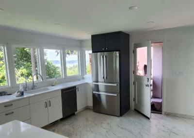 Kitchen workspace with stainless steel refrigerator, white cabinets, marble tile floor, and window views.