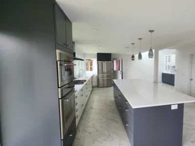 Mercer-Island-full-view-of-kitchen-remodel-project Open-concept kitchen with a large gray island, white quartz counters, double wall ovens, and marble tile flooring.