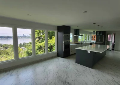Spacious kitchen with dark island, marble flooring, and large windows overlooking the water and Seattle skyline.