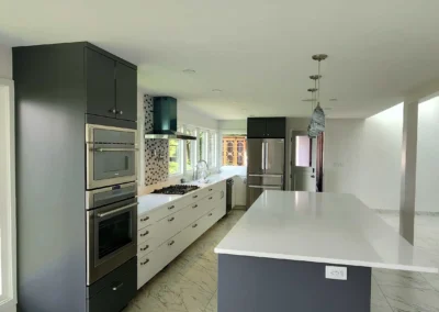 Modern kitchen with a dark gray island, white countertops, double wall ovens, and marble-veined tile flooring on Mercer Island.