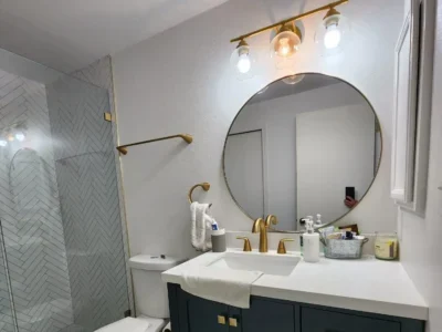 Seattle Bathroom Remodeling-Elegant Navy Vanity-and-Herringbone-Shower Seattle bathroom remodel featuring a navy vanity with gold hardware, a round mirror, modern lighting, and a herringbone tile shower.