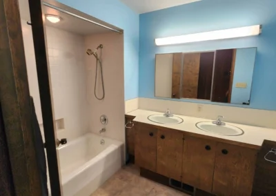 Original dated Mercer Island bathroom prior to layout overhaul, featuring a wood veneer double vanity, old fluorescent lighting bar, and an alcove tub shower setup.