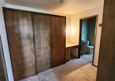 Original dated Mercer Island primary bathroom dressing area prior to layout overhaul, featuring legacy wood veneer closets, integrated built-in vanity desk, and old carpeting.