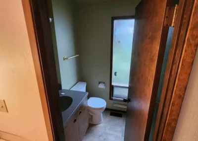 Original dated Mercer Island powder room prior to design-build transformation, featuring a legacy single vanity, old toilet setup, and weathered vinyl flooring.