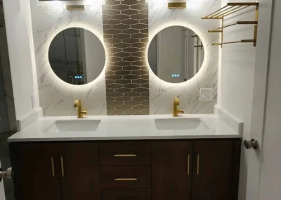 Tailored Mercer Island double vanity configuration featuring dark wood cabinetry, white quartz countertops, dual backlit circular mirrors, premium brushed gold fixtures, and an architectural accent tile backsplash.