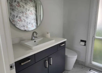 Mercer Island powder room transformation featuring a charcoal vanity, integrated white quartz countertop, structural round mirror, and marble-look porcelain tile flooring.