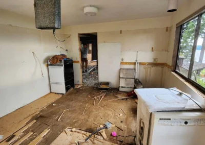 Gutted kitchen during demolition with exposed subfloor, debris, and window views on Mercer Island.