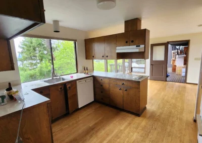 Dated wood kitchen with white countertops, sink under a window, and wood floors before remodeling.
