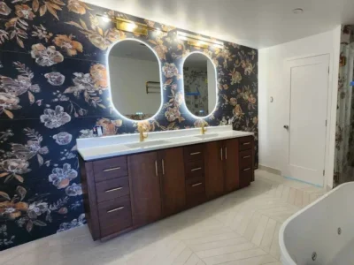 mercer-island-primary-bathroom-remodel-double-vanity-soaking-tub-scaled Bespoke Mercer Island primary bathroom suite featuring an expansive dark wood double vanity, illuminated oval mirrors, a floral statement wall, chevron flooring, and an integrated freestanding soaking tub.