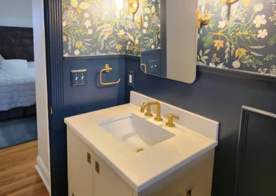 A bathroom vanity with gold hardware set against navy blue walls with integrated crown molding.