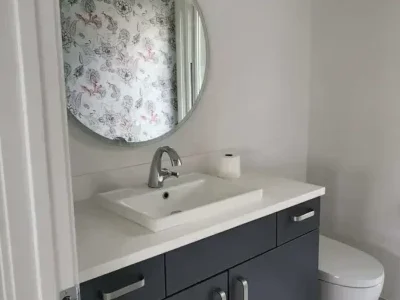 mercer-island-bathroom-remodel-floating-vanity Mercer Island powder room transformation featuring a charcoal vanity, integrated white quartz countertop, structural round mirror, and marble-look porcelain tile flooring.
