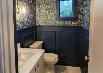 Navy blue picture frame wainscoting paired with floral botanical wallpaper and a white vanity in a luxury bathroom.