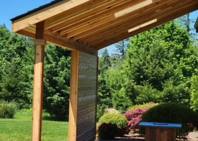 Exterior view of a cedar post-and-beam covered patio with a skylight and stamped concrete, surrounded by garden landscaping in Redmond