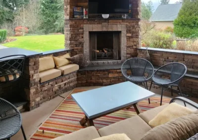 Covered Redmond patio lounge with a stacked stone fireplace, mounted TV, built-in bench seating, and outdoor furniture
