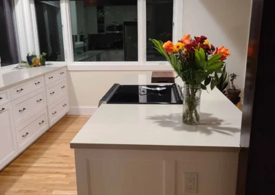 White peninsula with black cooktop and fresh flowers beside large windows in a Redmond kitchen