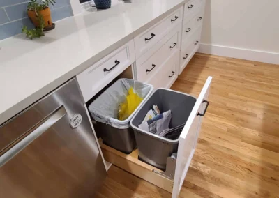 Hidden pull-out trash and recycling bins in a white cabinet in a Redmond kitchen remodel