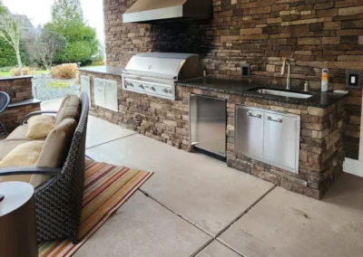 Redmond Outdoor Kitchen with Stacked Stone and Built-In Grill Alt: Redmond outdoor kitchen with stacked stone walls, a built-in stainless grill, granite counters, sink, and covered seating