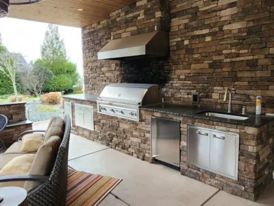 redmond-outdoor-kitchen-stone-grill-granite-counter Redmond outdoor kitchen with stacked stone walls, a built-in stainless grill, granite counters, sink, and covered seating